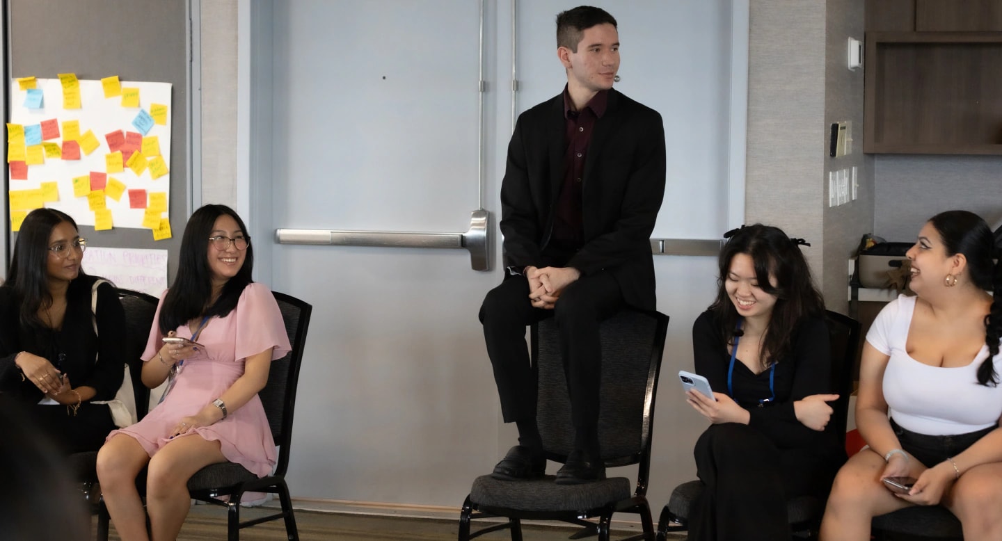 Rhizome fellows gathered in a circle as one student stands on a chair while speaking